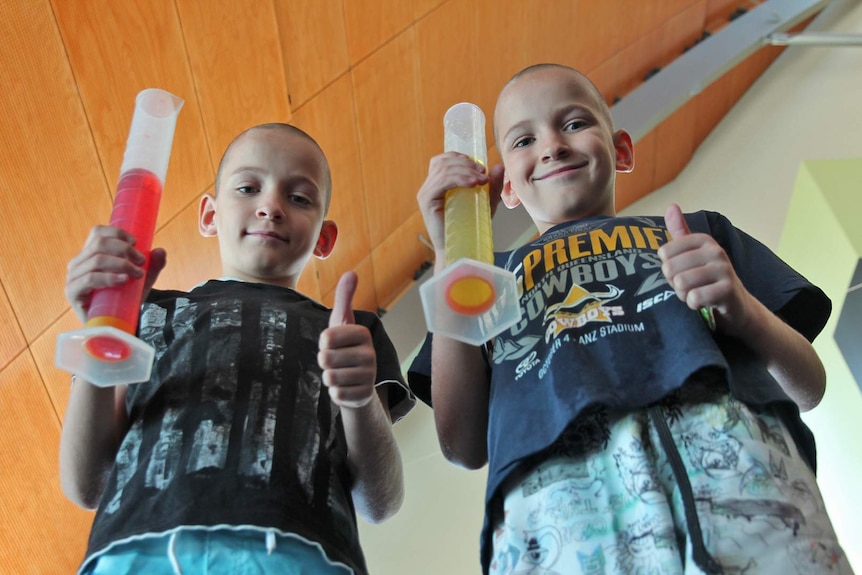 Two boys hold oversized test tubes and give the thumbs up gesture at a science show