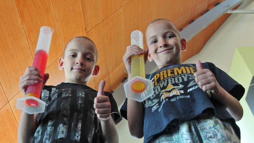 Two boys hold oversized test tubes and give the thumbs up gesture at a science show