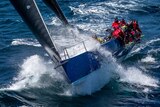 Crew members in red jackets race a blue and white yacht at sea