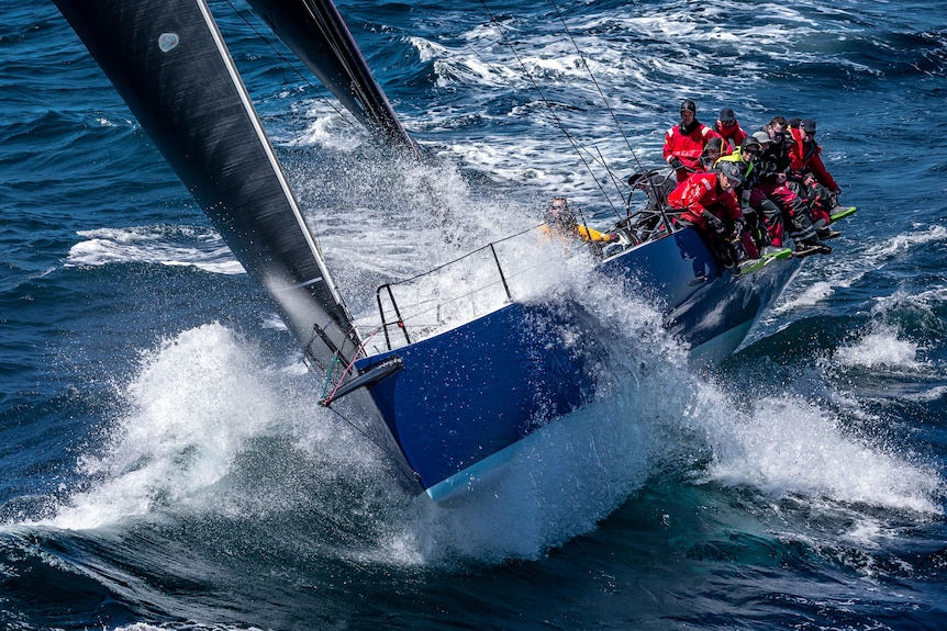 Crew members in red jackets race a blue and white yacht at sea