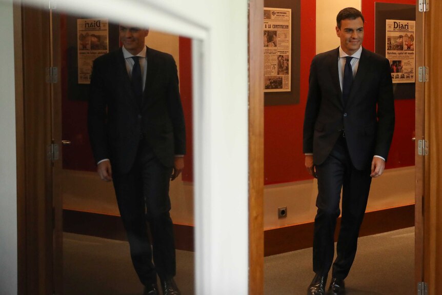 Pedro Sanchez is seen talking into a room, his image reflected on a mirror.