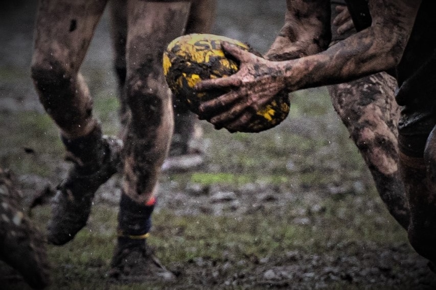 Unidentified AFL player holding the ball on a muddy playing field.