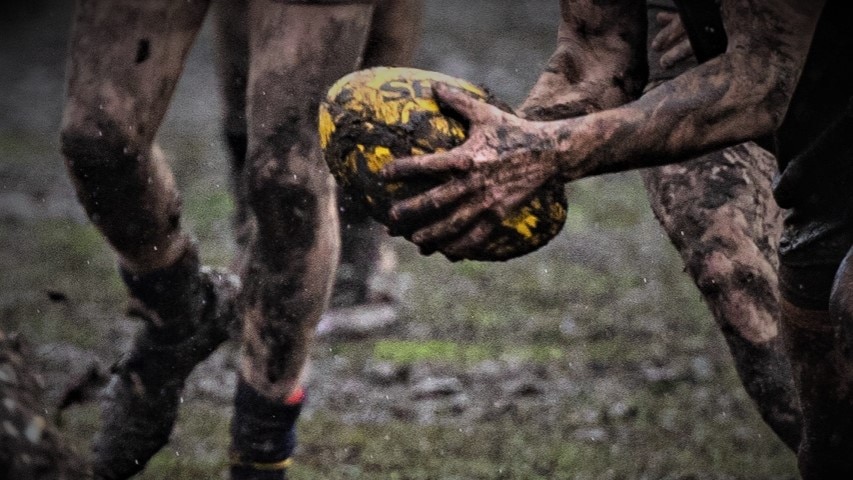 Unidentified AFL player holding the ball on a muddy playing field.