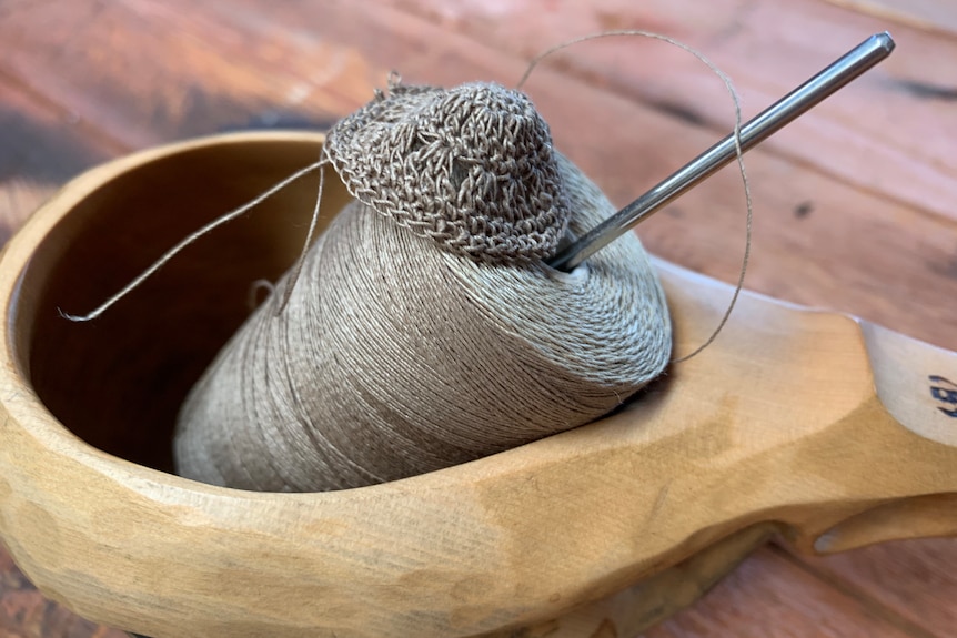 Needle and thread perched in a wooden dish with stitched crochet button.