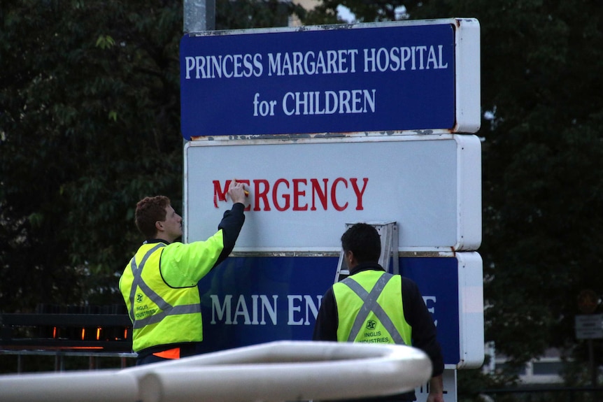 Two men in hi-vis clothing take down an emergency department decal on a Princess Margaret Hospital sign.