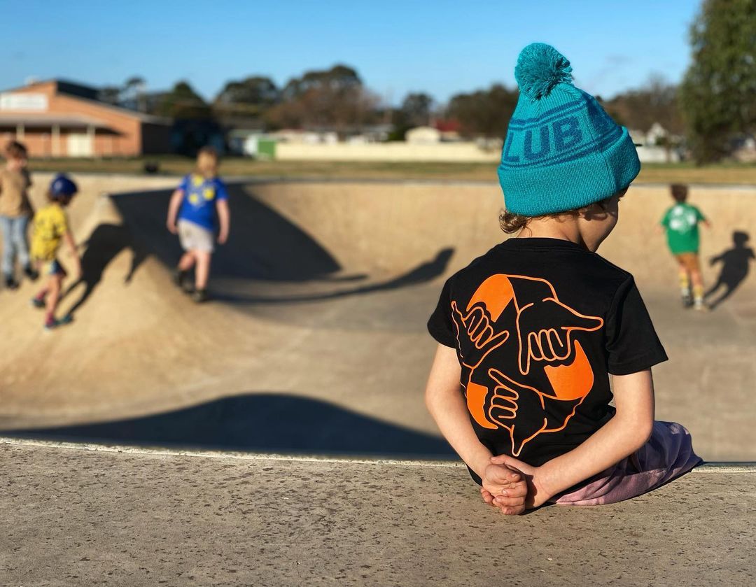 A child in a Gnarly Neighbours shirt sits on the skateramp, their back facing towards the camera.
