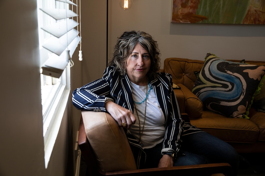 A woman with a black and white striped shirt and black, greying hair sits on a couch.
