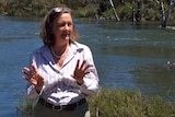 A woman speaking and standing in front of a river.