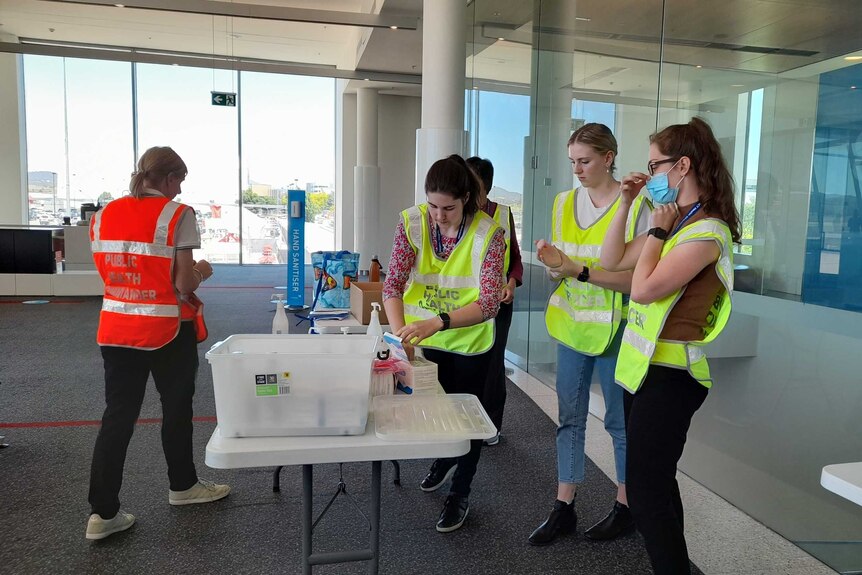 Public health workers set up a table at an arrival gate.