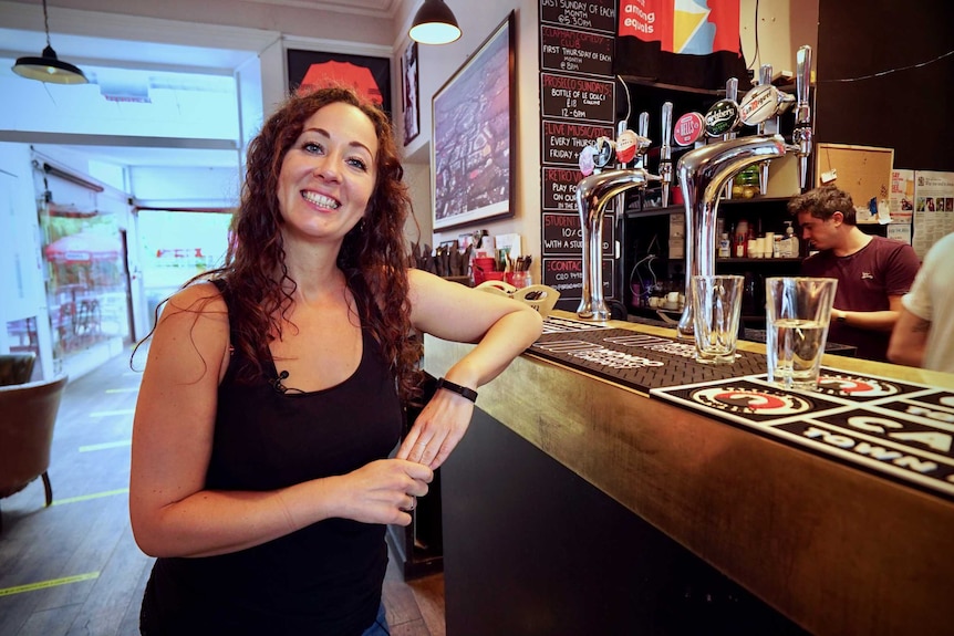 A woman leans on the bar of a pub while smiling at the camera.