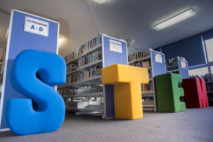 Big fabric letters in blue, yellow, green and red spelling STEM in front of aisle of a school library