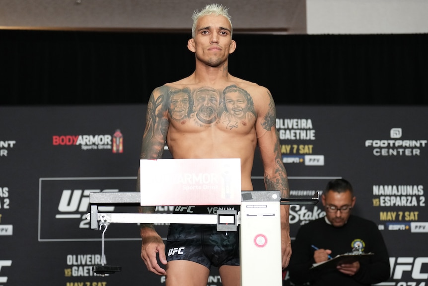 Charles Oliveira looks serious while standing shirtless on the scales