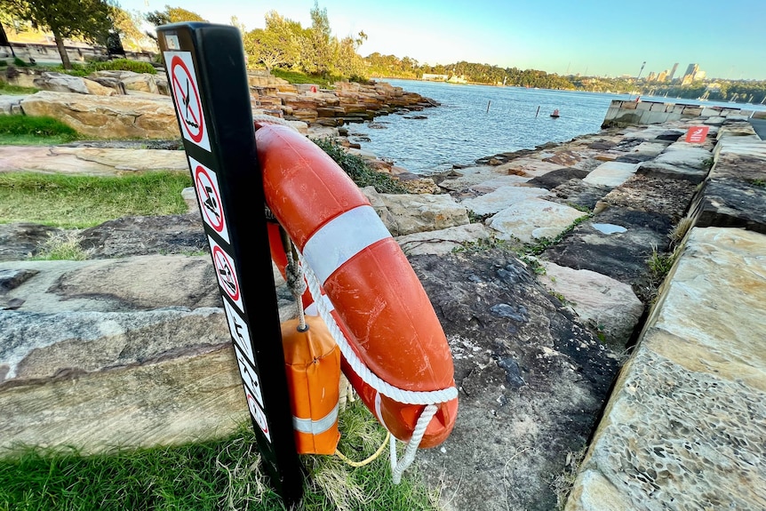A sign next to a life buoy next to Sydney Harbor