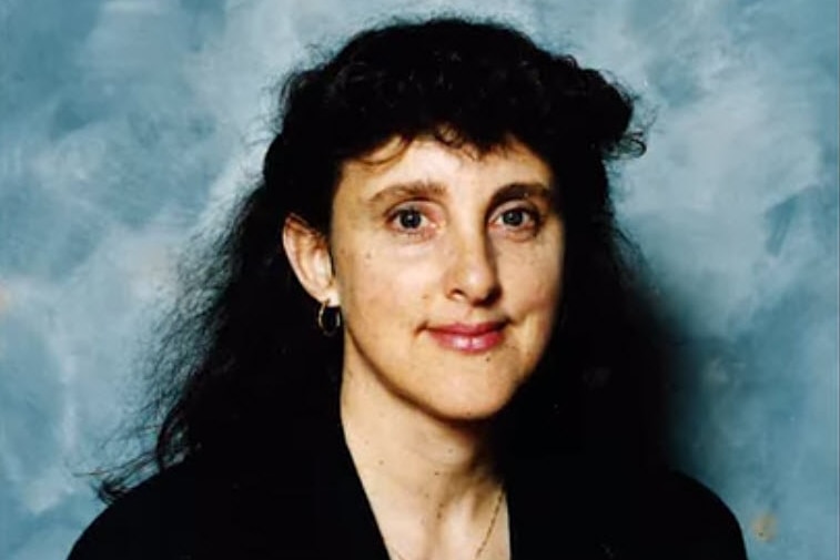 A woman with black hair stands in front of a blue wall.