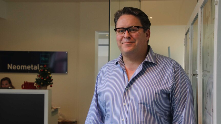 Neometals managing director Chris Reed stands and smiles with the company's reception area in the background.