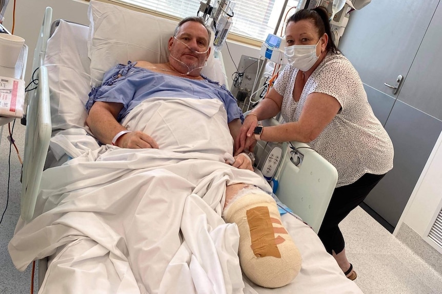 Greg and Elizabeth Hislop in hospital. Greg is in bed with his amputated leg bandaged.