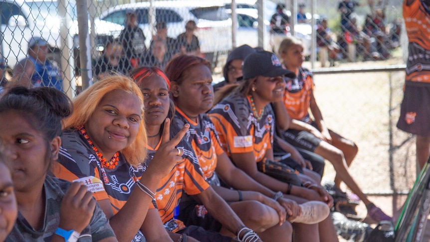 A female softball team sits on a bench, watching the game.