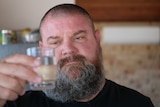 A man with a beard and a shirt cropped hair holds up a glass of water