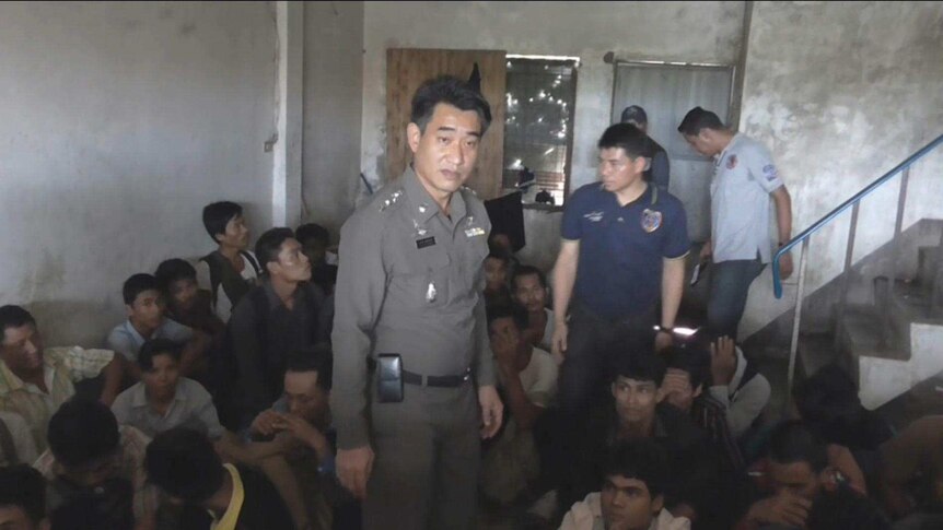 A Thai police officer stands with a group of people from Myanmar, apparently left by smugglers on the Thai-Malaysian border.