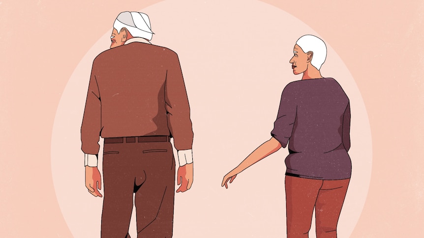 An old man and woman stand together. The woman reaches her hand towards the man but he turns away