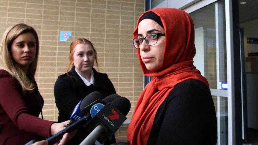 Ms Kandemir wears a red head scarf and speaks into microphones.