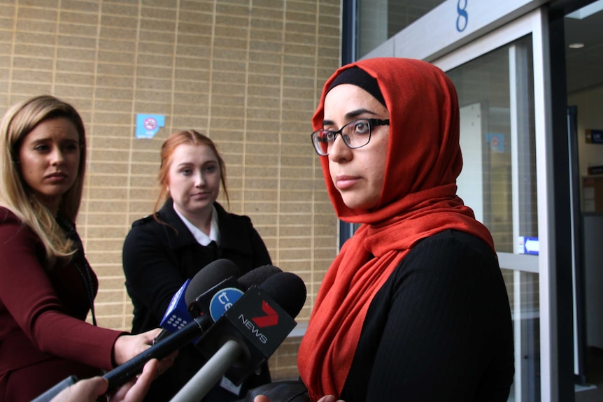 Ms Kandemir wears a red head scarf and speaks into microphones.