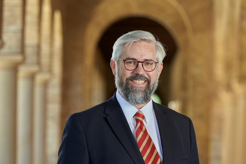 A man in a suit and glasses smiles at the camera.