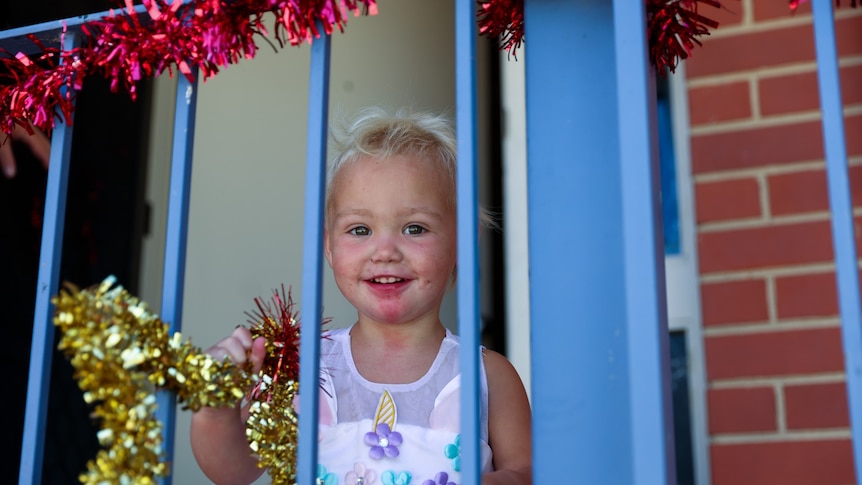 A two year old child hanging tinsel from a balcony.
