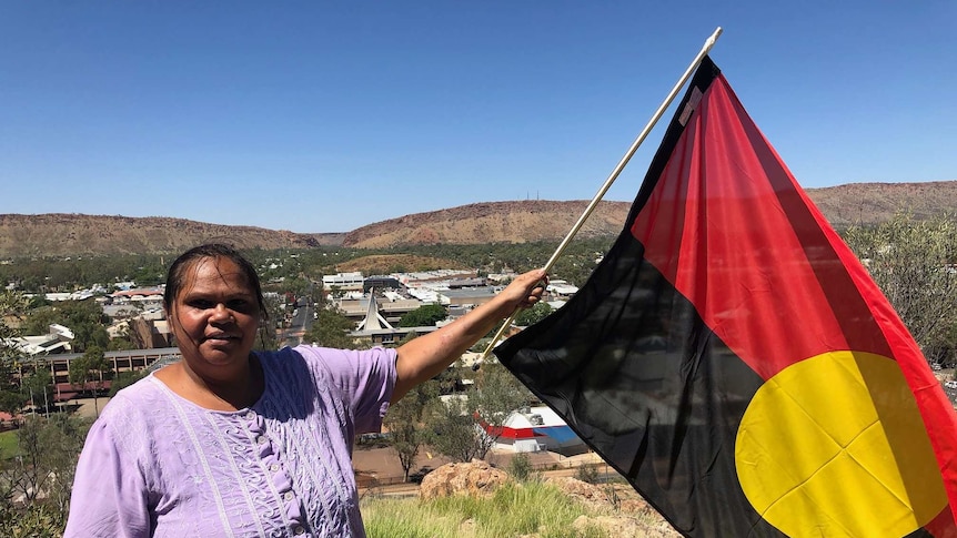 An Indigenous woman holds the Aboriginal flag on top of Anzac Hill in Alice Springs.