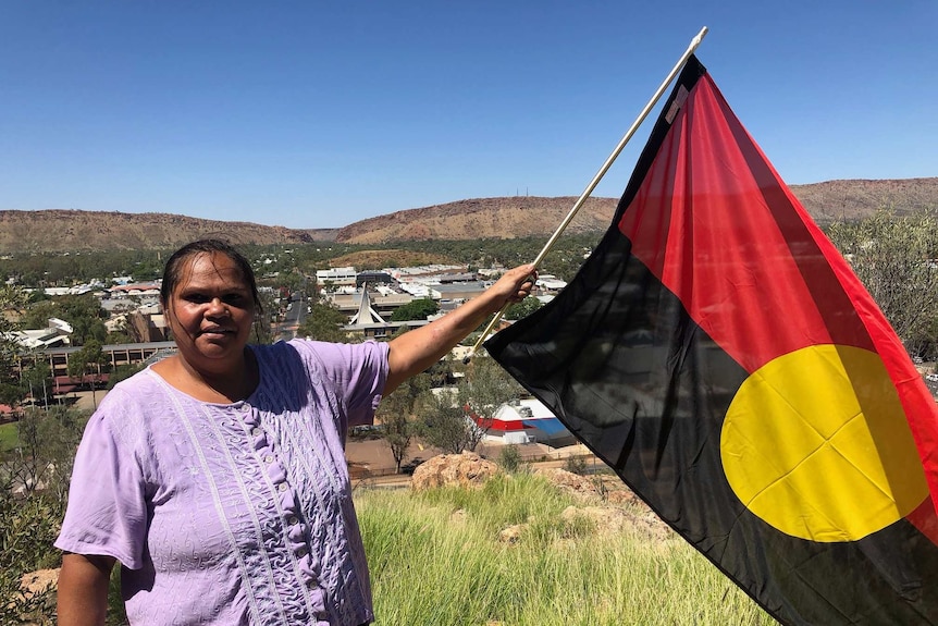 An Indigenous woman holds the Aboriginal flag on top of Anzac Hill in Alice Springs.