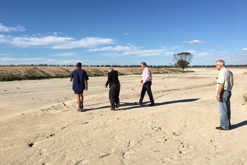 Lady and three men walk across sand filled dam