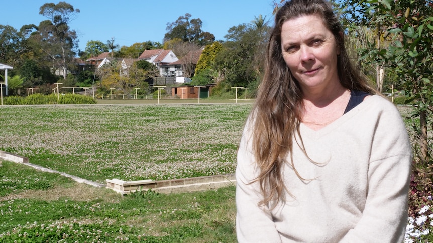 A woman in front of an overgrown disused lawn bowls field.