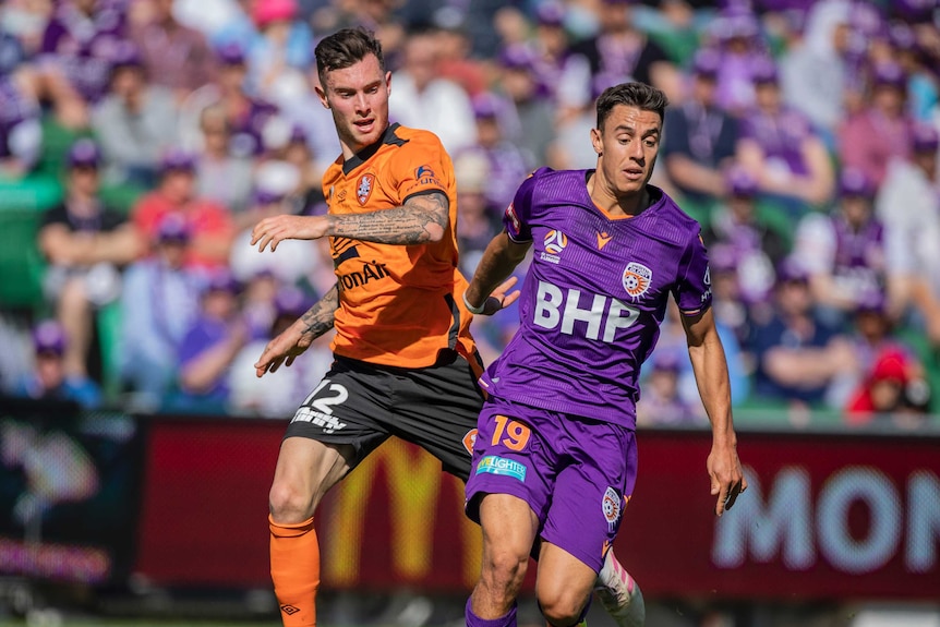 Chris Ikonomidis, right, runs behind Aiden O'Neill who is dribbling the ball. The crowd is seen in the background.