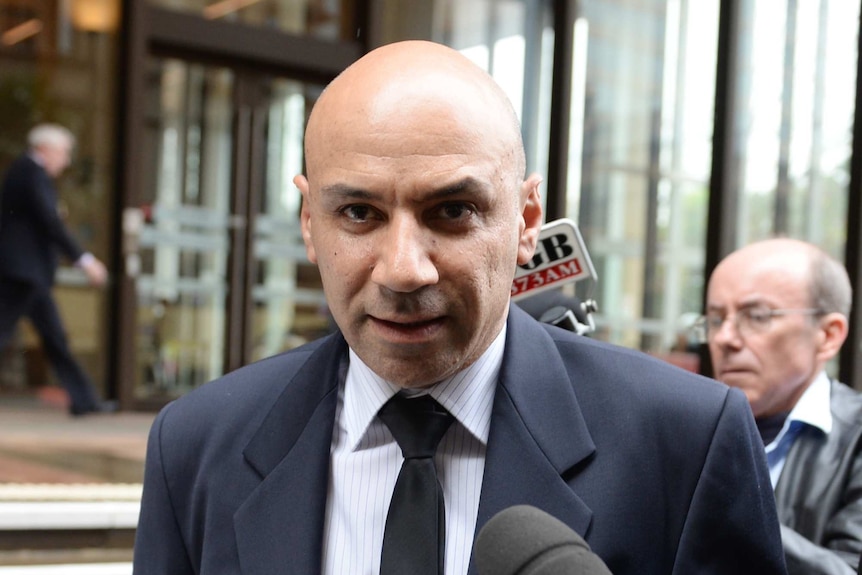 A man in a suit walks past journalists holding out microphones. 