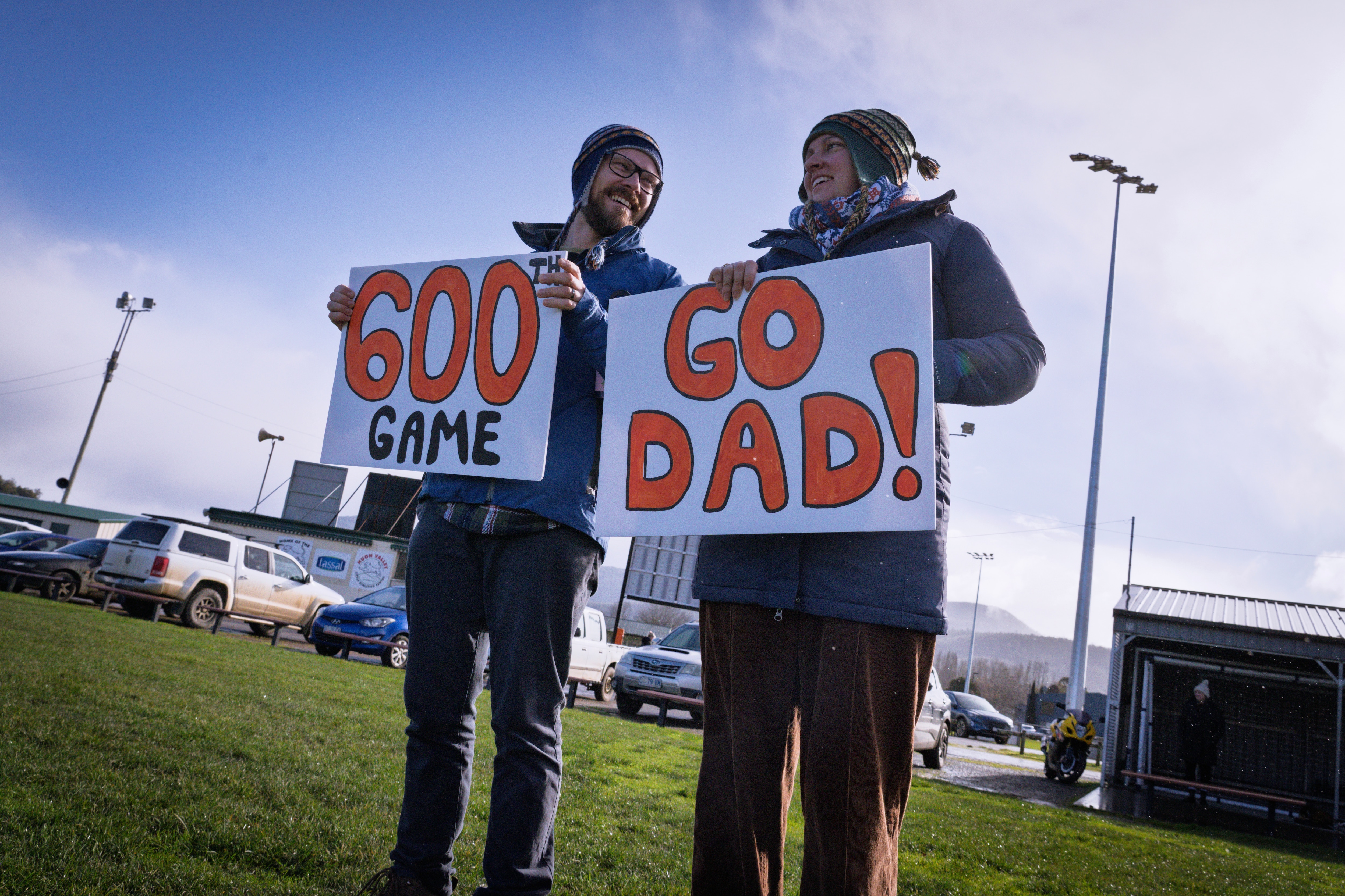 A man and woman hold signs saying 'Go Dad' on the side of a soccer pitch.