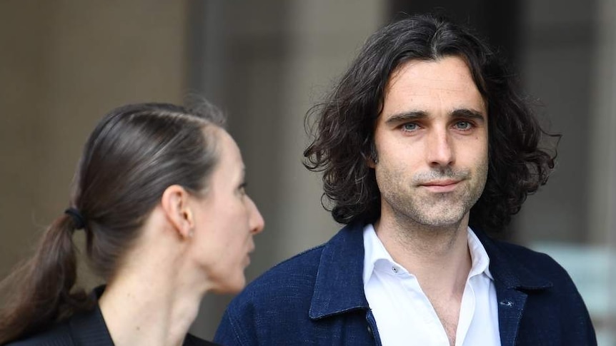 man with long black hair walking with woman holding clipboard