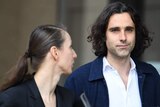man with long black hair walking with woman holding clipboard
