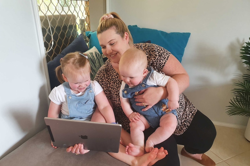 A woman with a baby and a toddler on her lap looking at a screen