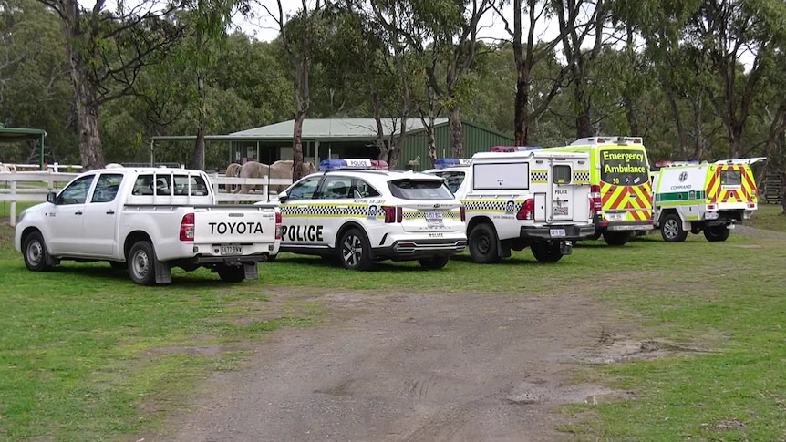 A ute, police cars and ambulances on lawn near stables