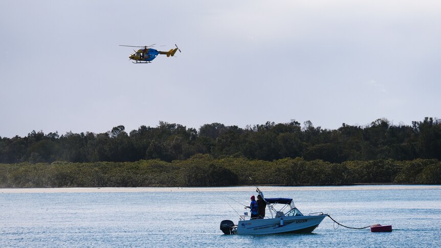 A maritime boat on a lake and a helicopter flying in the sky nearby,
