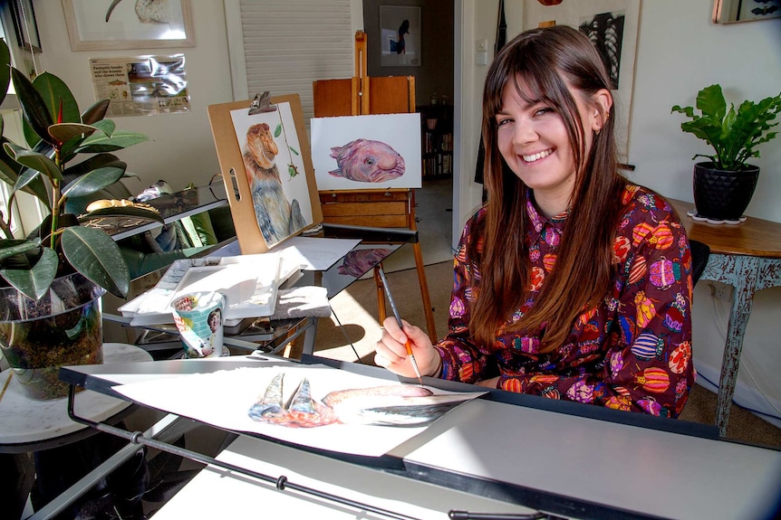 A young woman holding a paint brush surrounded by illustrations of so-called ugly animals