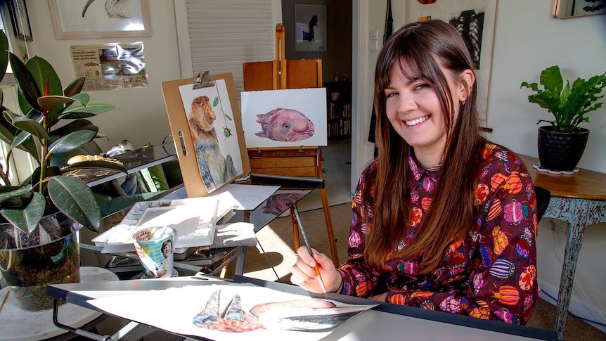A young woman holding a paint brush surrounded by illustrations of so-called ugly animals