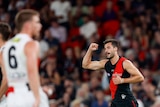 An Essendon player raised his clenched fist in celebration as a St Kilda defender looks on.