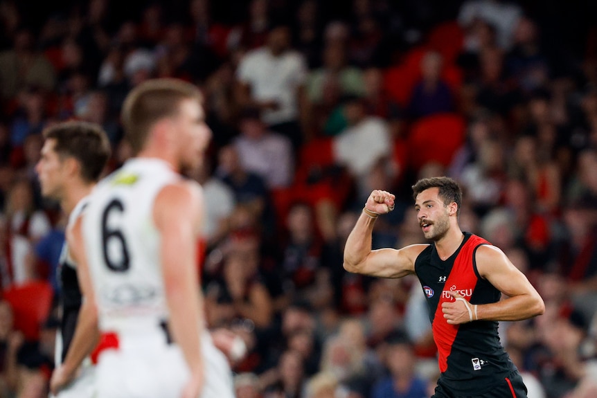 An Essendon player raised his clenched fist in celebration as a St Kilda defender looks on.
