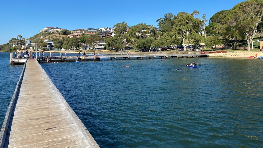 A scenic photo of a jetty near a stretch of coastline with people on it fishing and swimming.