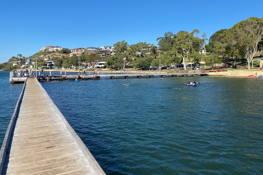 A scenic photo of a jetty near a stretch of coastline with people on it fishing and swimming.