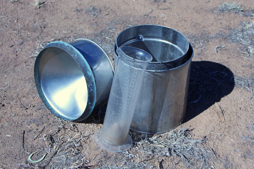 An empty rain gauge sitting on dry dirt