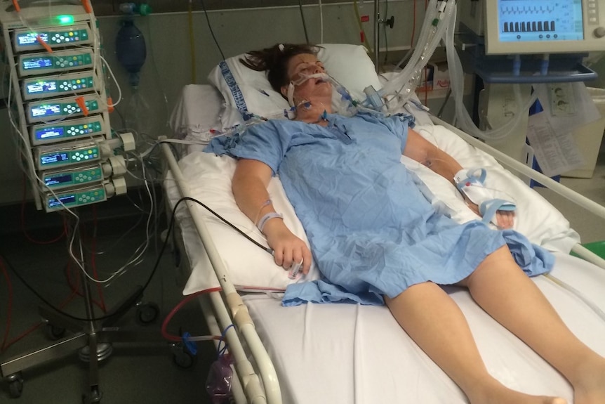 A woman in a blue gown on a ventilator in hospital.