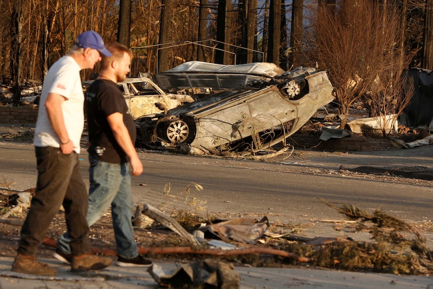 Residents walk past a blackened car tipped over