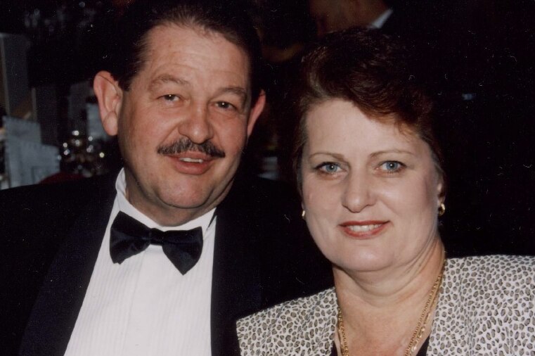 A man and a woman in formal dress smile at the camera, looking happy.